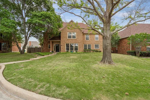 a large tree in front of a brick house with a big yard