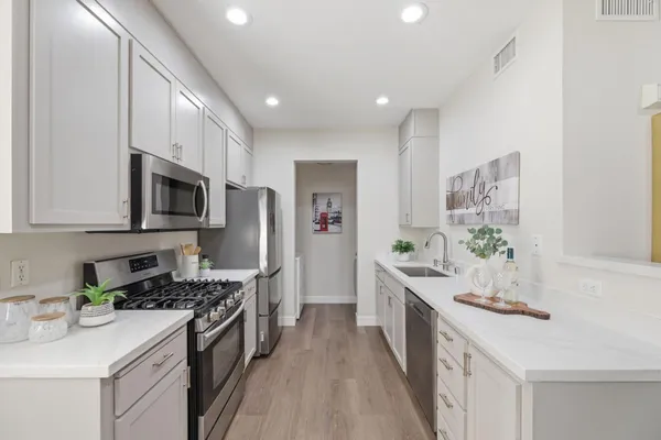 a kitchen with stainless steel appliances a stove top oven a sink a refrigerator white cabinets and wooden floor