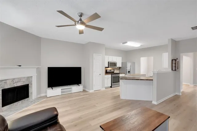 a living room with stainless steel appliances furniture a fireplace a flat screen tv and white cabinets
