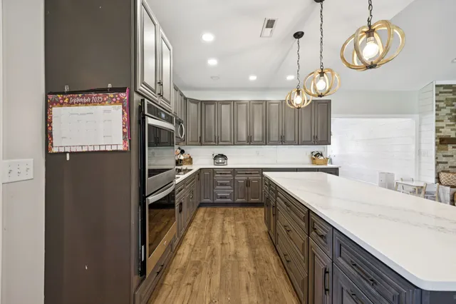 a large kitchen with stainless steel appliances kitchen island granite countertop a sink a stove and a wooden floors