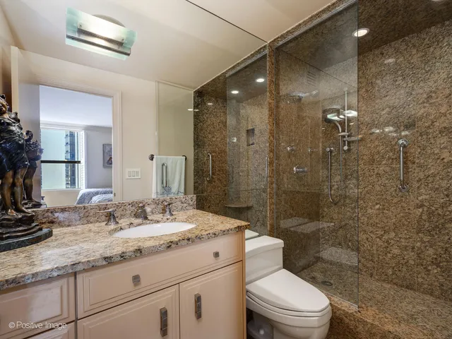 a bathroom with a granite countertop sink a toilet a mirror and shower