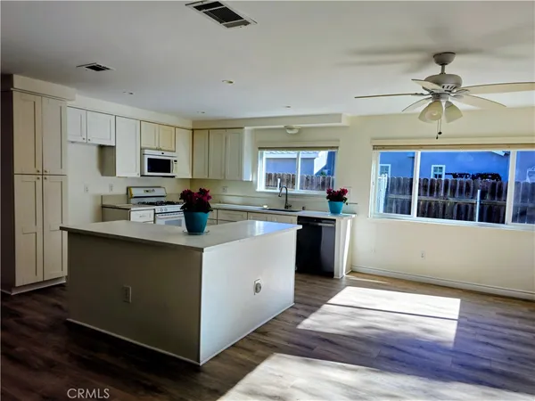 a kitchen with stainless steel appliances kitchen island granite countertop a refrigerator a stove top oven a sink dishwasher and white cabinets with wooden floor