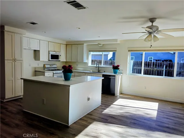 a kitchen with stainless steel appliances kitchen island granite countertop a refrigerator a stove top oven a sink dishwasher and white cabinets with wooden floor