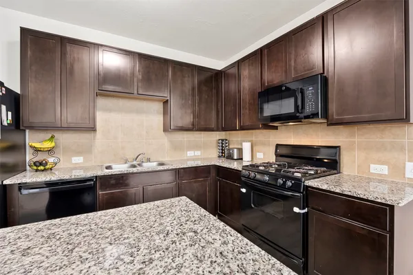 a kitchen with kitchen island granite countertop stainless steel appliances wooden cabinets a stove top oven a sink and dishwasher