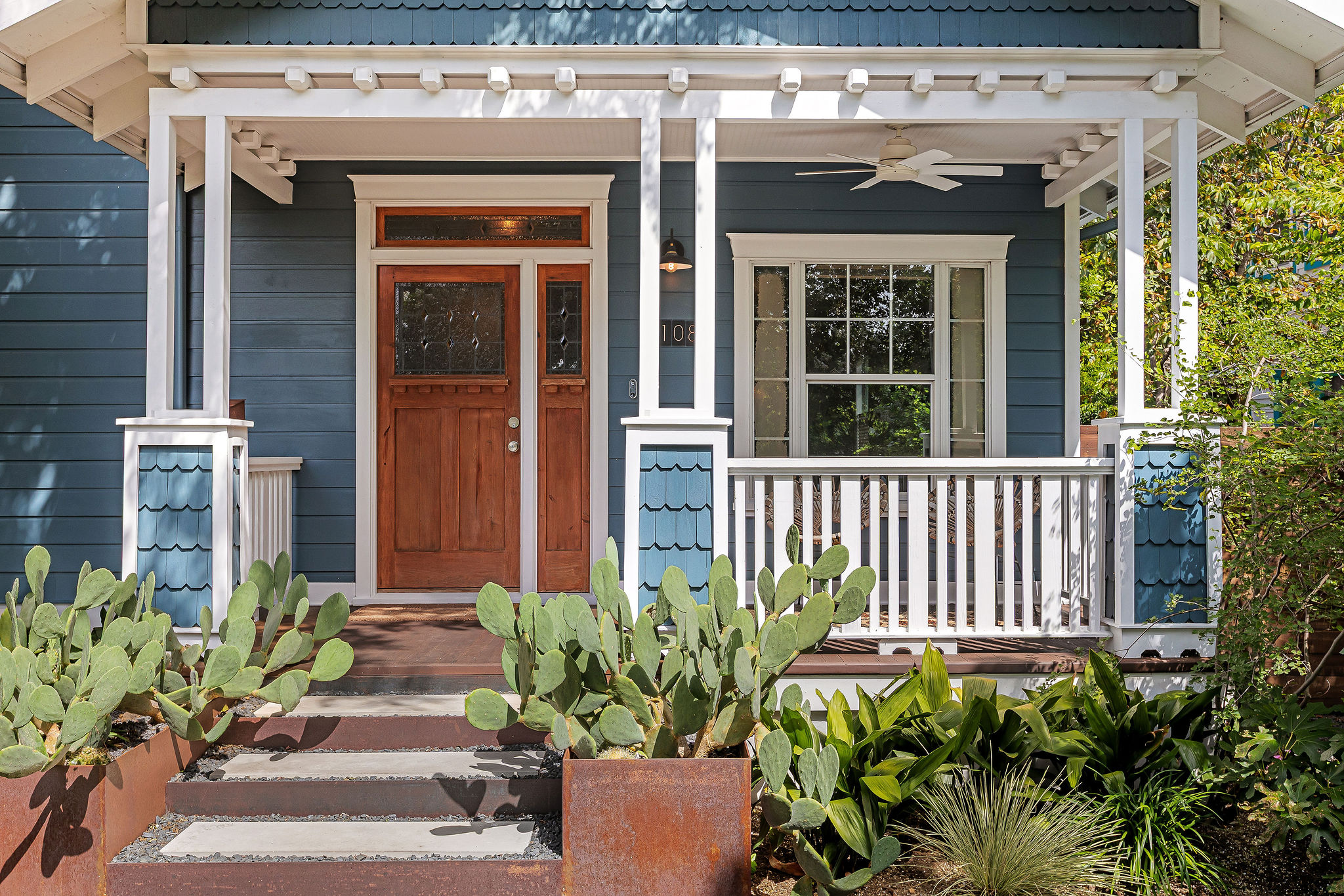 5108 Eilers Avenue Austin, TX 78751 - Photo 28 of 39 A charming blue craftsman home features a welcoming front porch framed by mature trees and desert landscaping.