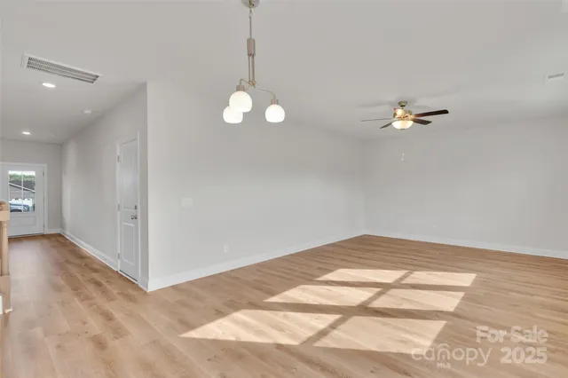 a view of an empty room with a chandelier fan and kitchen view