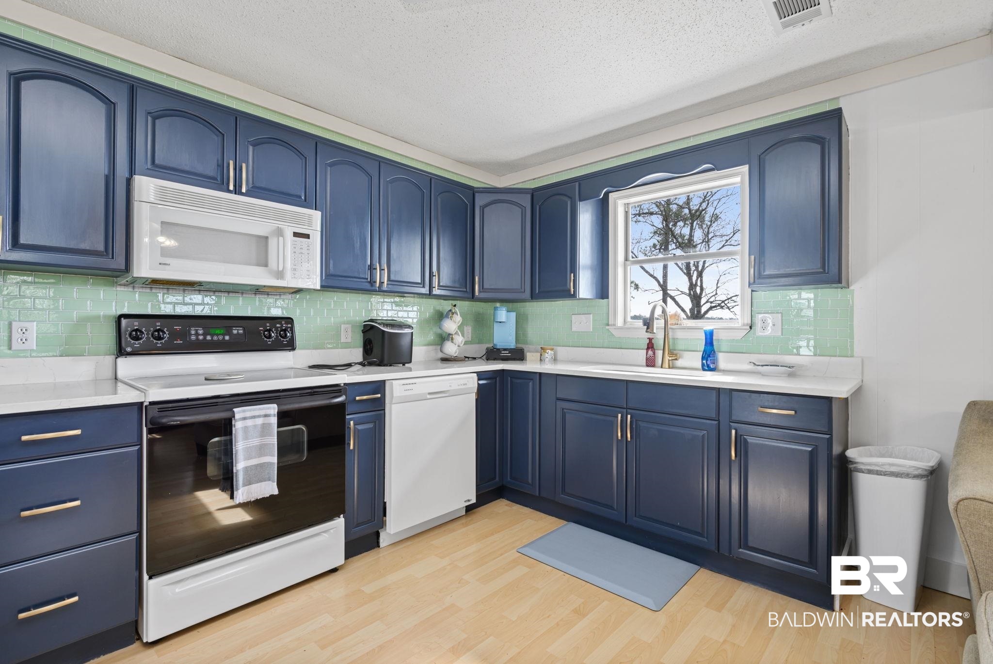 7947 Bayshore Drive Elberta, AL 36530 - Photo 17 of 26 Kitchen featuring blue cabinetry, white appliances, decorative backsplash, a textured ceiling, and light wood-type flooring