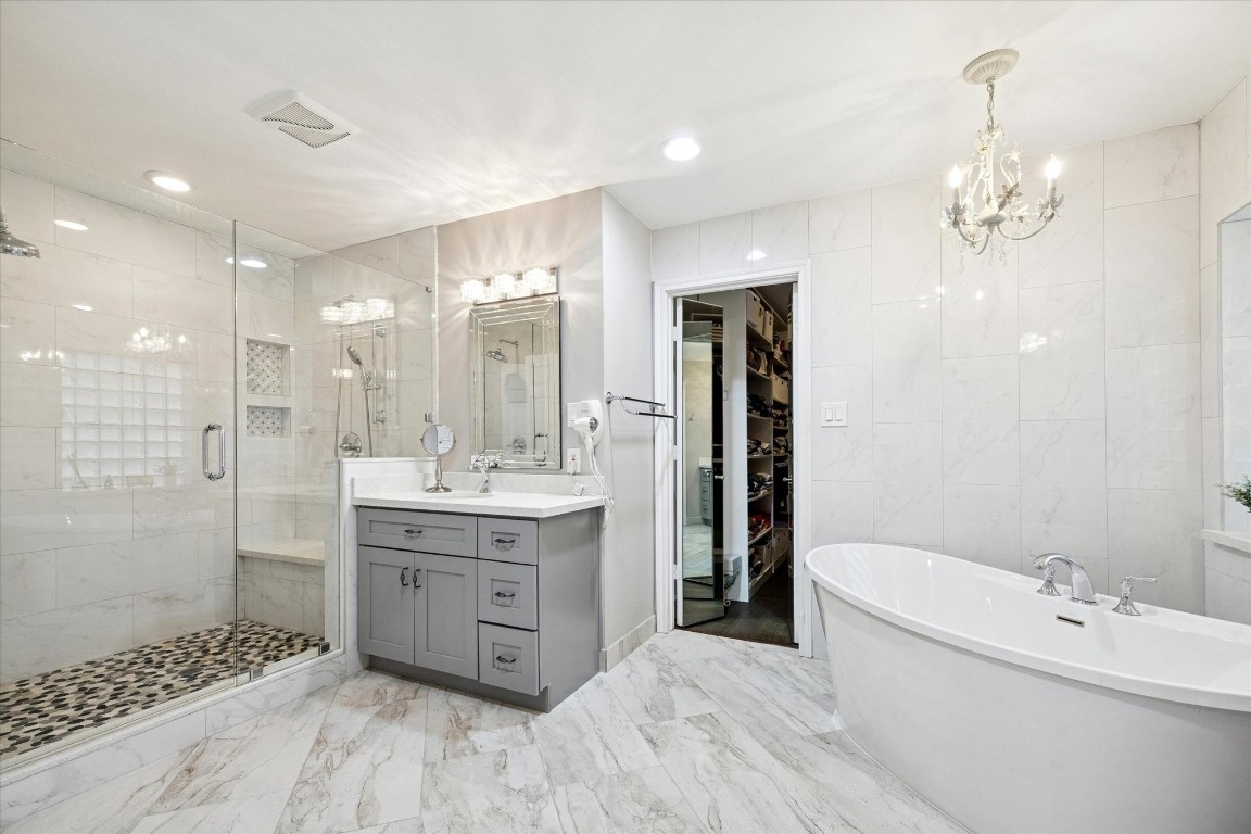 Luxury meets functionality in this renovated home. This beautiful primary en-suite bathroom features a spacious glass-enclosed shower with intricate tile work, double, modern vanities with ample storage, and a freestanding bathtub. It includes elegant lighting fixtures and a walk-in closet, all set against a backdrop of polished ceramic tiles for a sophisticated look.