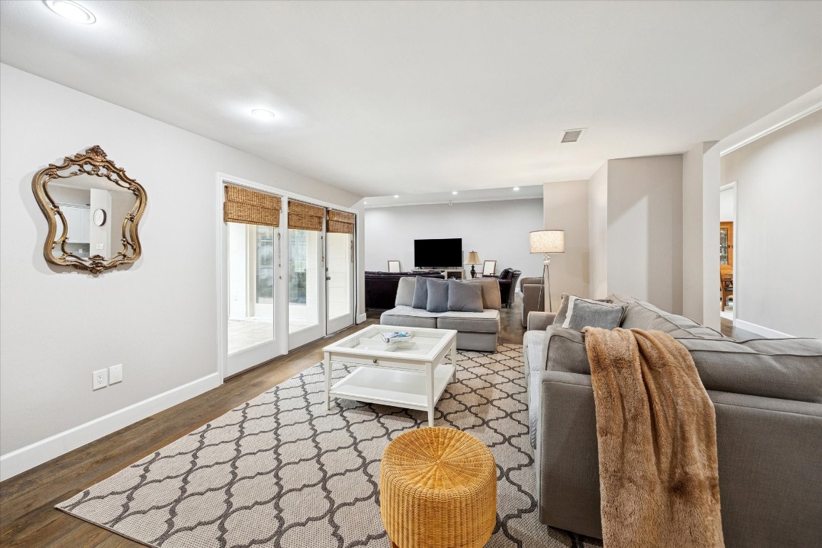 242 Vanderpool Lane Houston, TX 77024 - Photo 16 of 45 This photo showcases a spacious and inviting living room with neutral tones. Large windows and french doors with woven blinds allow natural light to fill the room, and there's a cozy living room off the family room, creating a perfect space for relaxation and entertainment.