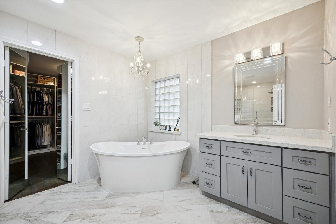 242 Vanderpool Lane Houston, TX 77024 - Photo 25 of 45 This elegant bathroom features a freestanding soaking bathtub, modern gray vanity with ample storage, and a stylish chandelier. The room is bright with tiled walls and floors, and it includes a spacious walk-in closet.