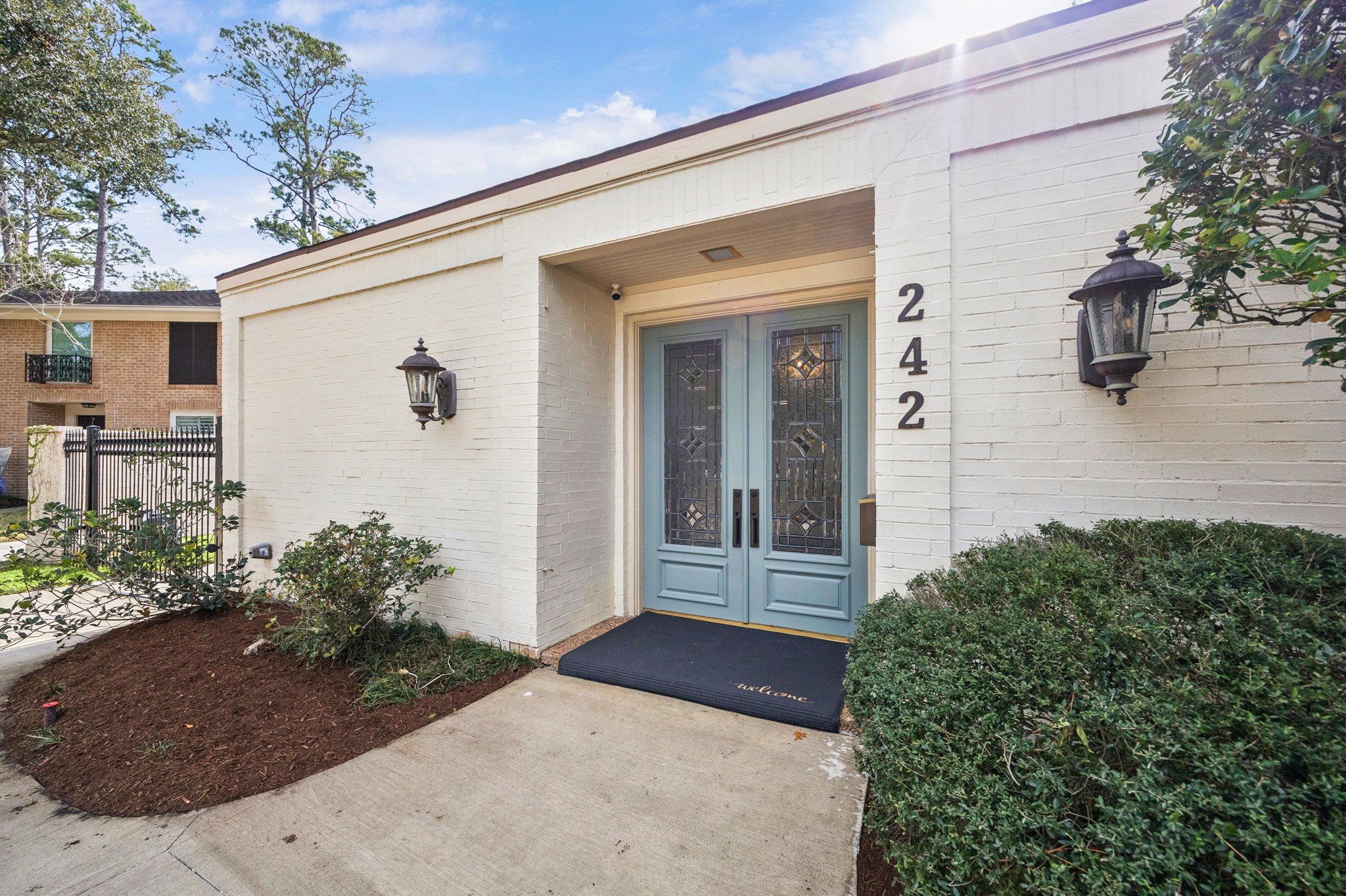 242 Vanderpool Lane Houston, TX 77024 - Photo 4 of 45 Enchanging light blue double doors and decorative glass, set in a white brick exterior. Features welcoming lantern-style lights and neat landscaping, creating an inviting first impression. This low maintence yard is a must have for our busy lifestyles.