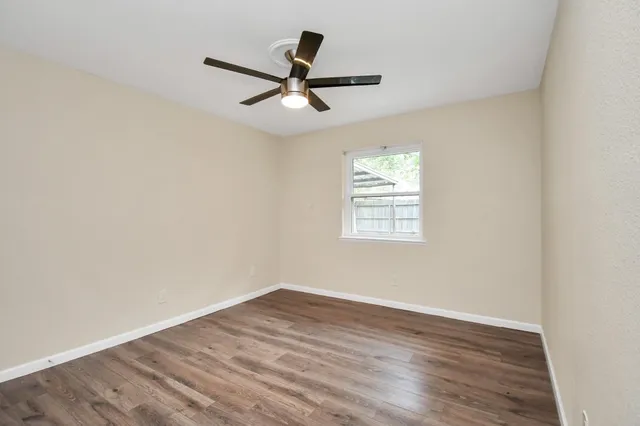 an empty room with wooden floor ceiling fan and windows