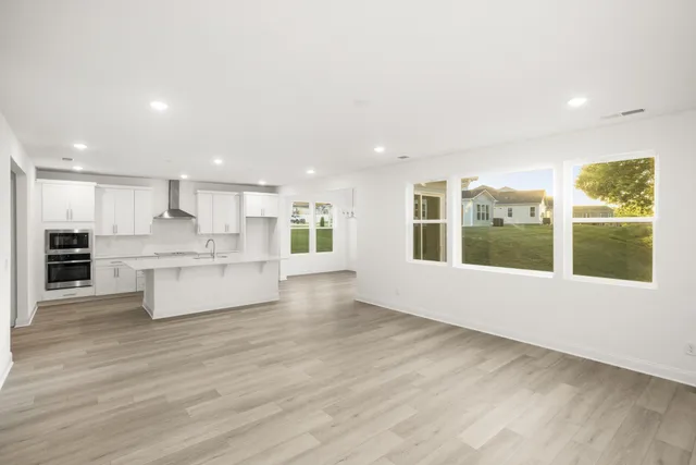 a large white kitchen with stainless steel appliances kitchen island granite countertop a large cabinets and a wooden floor