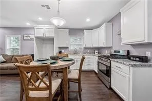 a kitchen with stainless steel appliances granite countertop a stove top oven a refrigerator a sink a dining table and chairs with wooden floor