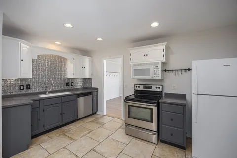 a kitchen with a sink a refrigerator and a stove top oven with white cabinets