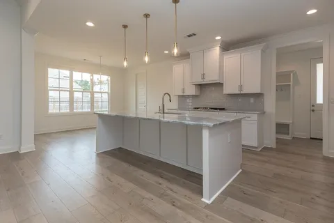a kitchen with stainless steel appliances granite countertop a sink a stove a refrigerator and white cabinets with wooden floor