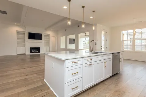a large white kitchen with a large island oven a sink dishwasher and a fireplace with wooden floor