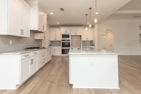 a large kitchen with granite countertop a white stove top oven and white cabinets
