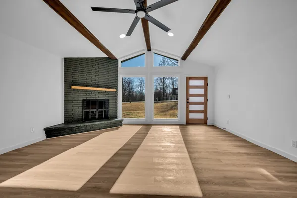 a view of an empty room with wooden floor fireplace and a window