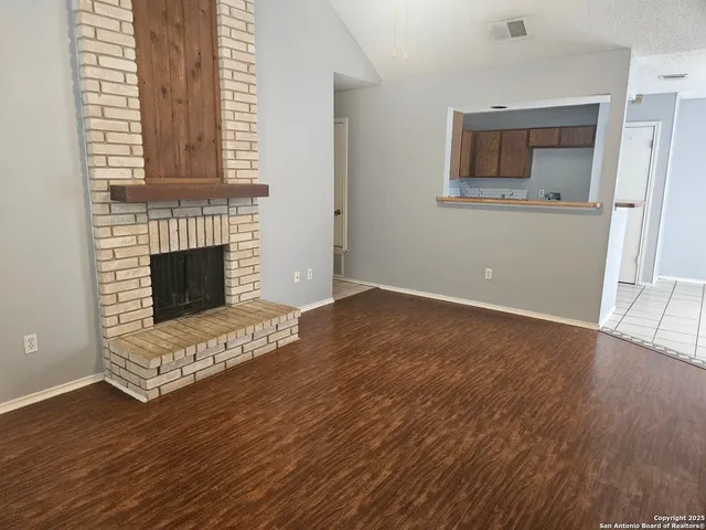 a view of an empty room with wooden floor and a fireplace