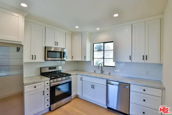 a kitchen with granite countertop white cabinets appliances a sink and a window