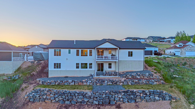 851 Grandview Drive Morgan, UT 84050 - Photo 56 of 68 Two-story residence featuring a white stucco exterior with a dark shingle roof, upper-level balcony with white railings, a lower-level patio, and tiered rock retaining walls