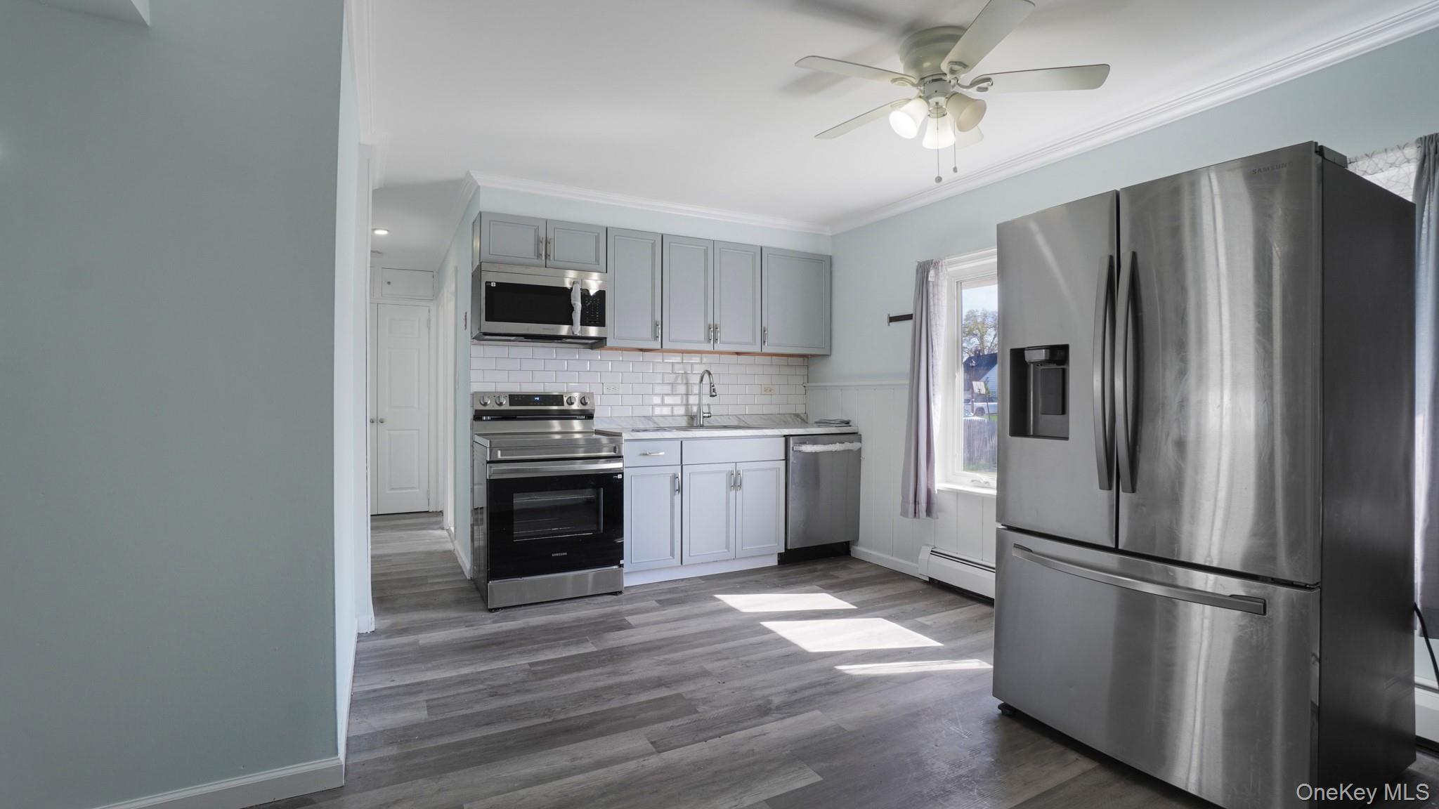 63 Blacksmith Road Levittown, NY 11756 - Photo 9 of 25 Kitchen featuring stainless steel appliances, light gray cabinetry, white subway tile backsplash, and wood-finish flooring