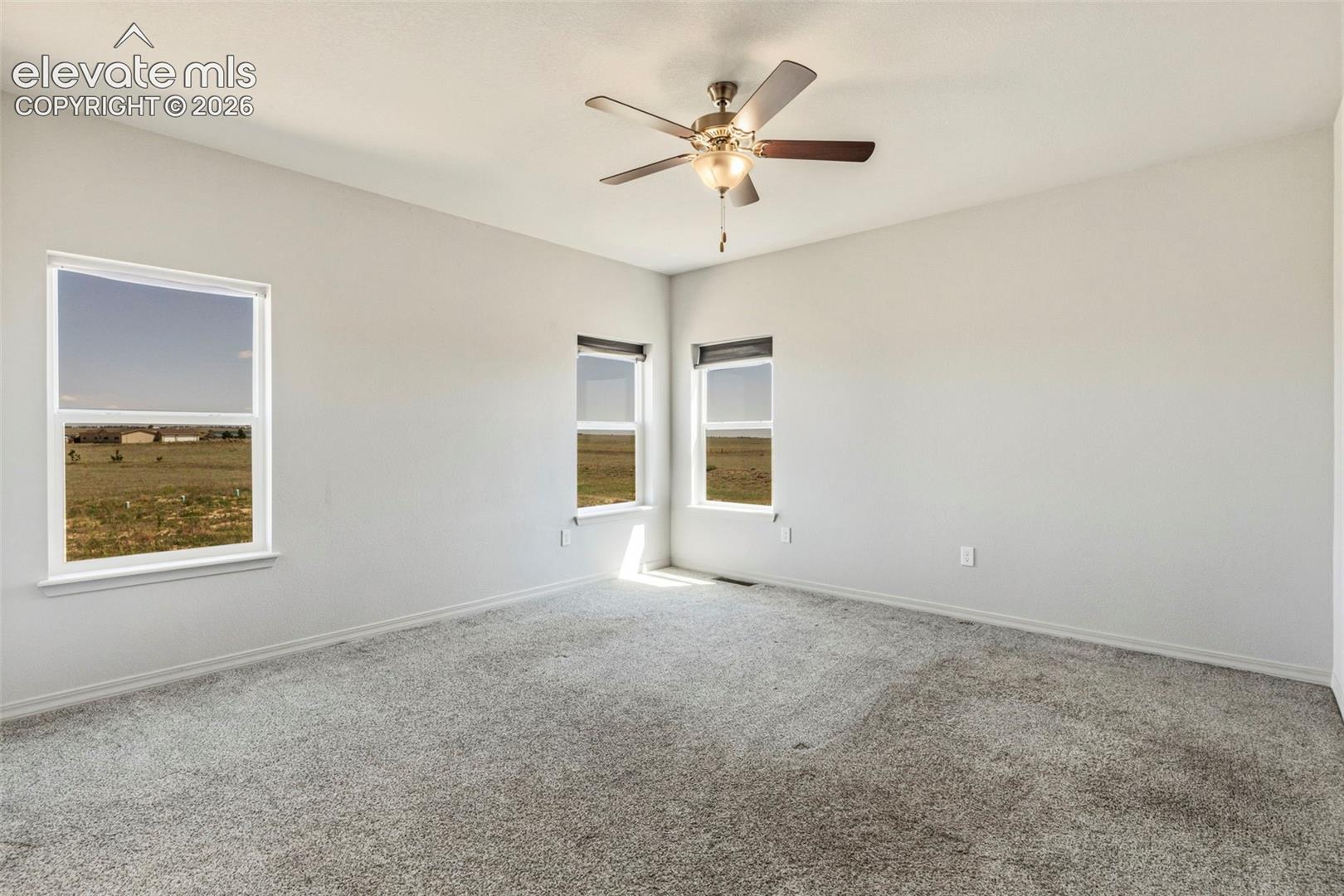 3955 North Yoder Road Yoder, CO 80864 - Photo 20 of 38 Spacious room featuring light gray carpeting, multiple windows providing natural light, a ceiling fan with integrated lighting, and neutral wall tones