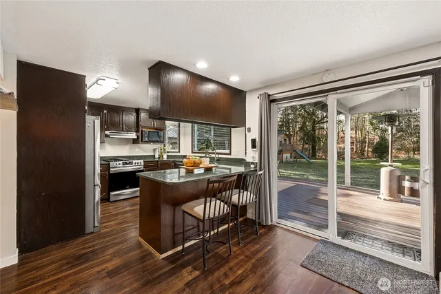 a kitchen with kitchen island granite countertop a stove a refrigerator a sink and a dining table with wooden floor