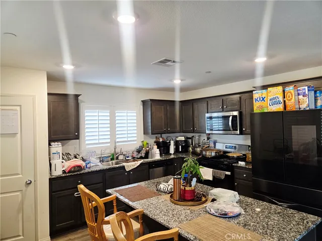 a kitchen with stainless steel appliances kitchen island granite countertop a refrigerator dining table and chairs