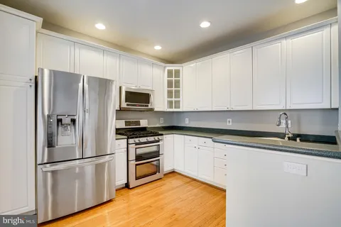 a kitchen with stainless steel appliances granite countertop a refrigerator a stove a sink and white cabinets