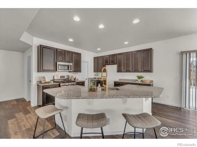 a kitchen with stainless steel appliances granite countertop a stove a sink a refrigerator white cabinets and couches with wooden floor