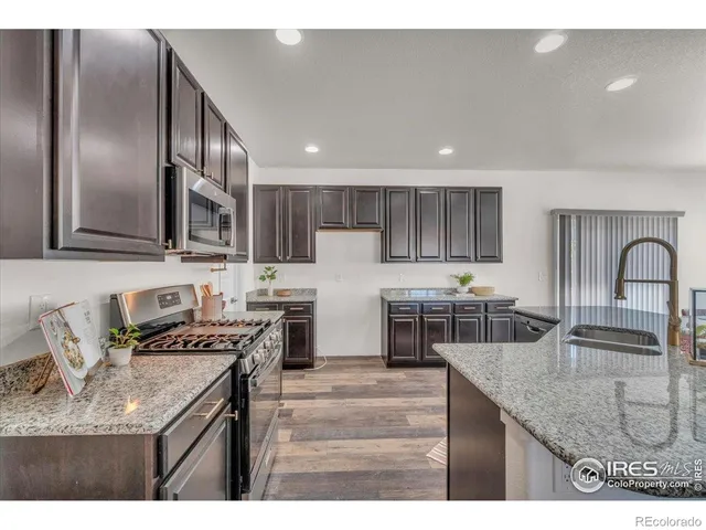 a kitchen with stainless steel appliances granite countertop a sink a stove and a refrigerator with wooden floor