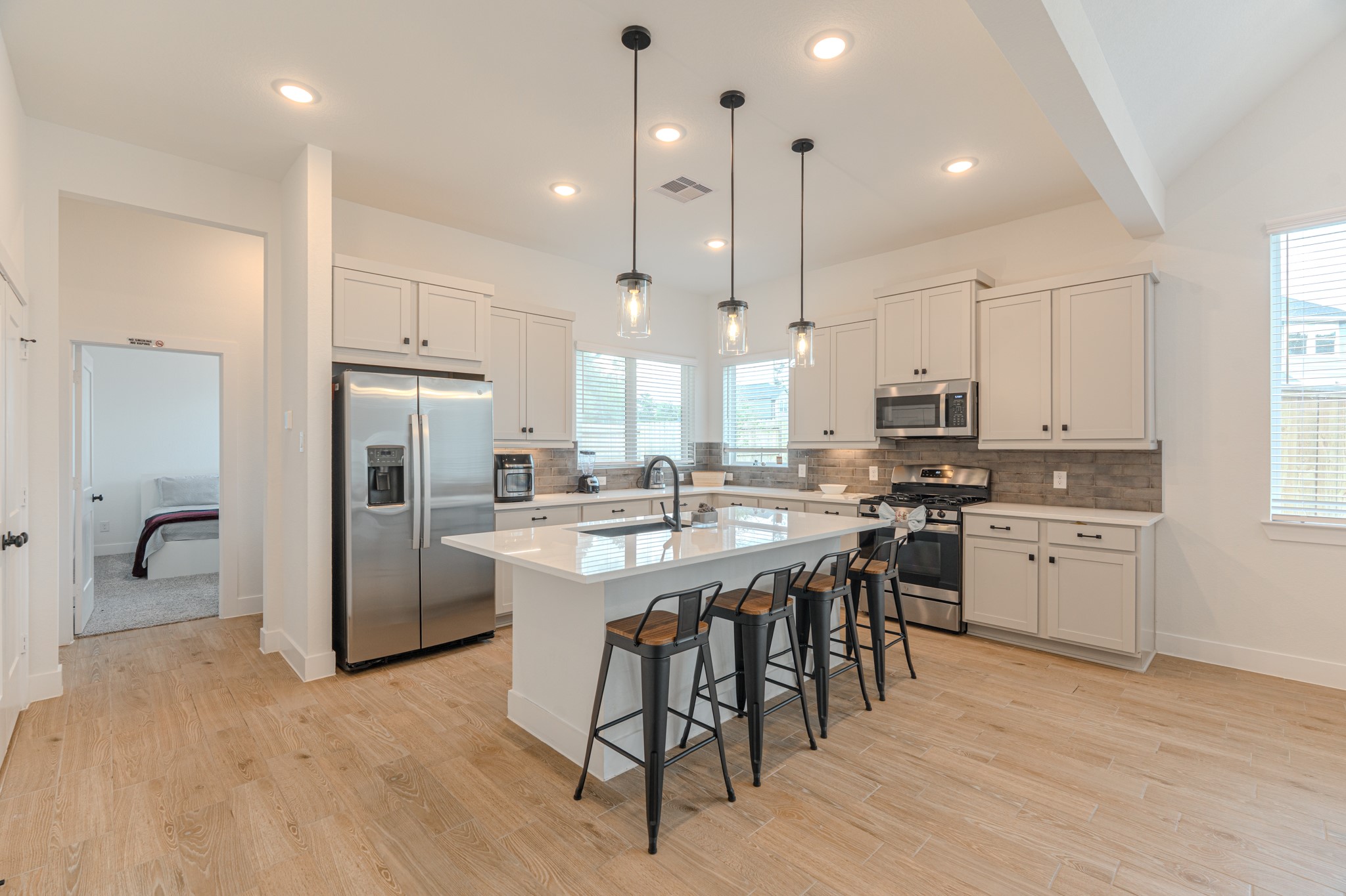 a kitchen with stainless steel appliances kitchen island granite countertop a refrigerator a stove a sink and white cabinets with wooden floor