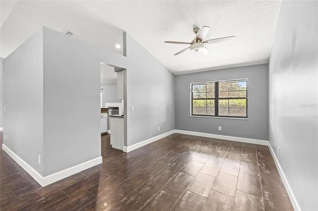 an empty room with wooden floor chandelier fan and windows