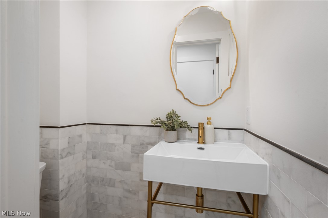 22625 Rye Road Shaker Heights, OH 44122 - Photo 17 of 38 Corner vanity featuring a white basin with a gold-tone faucet, a gold-framed mirror, and marble-look wainscoting with a dark trim