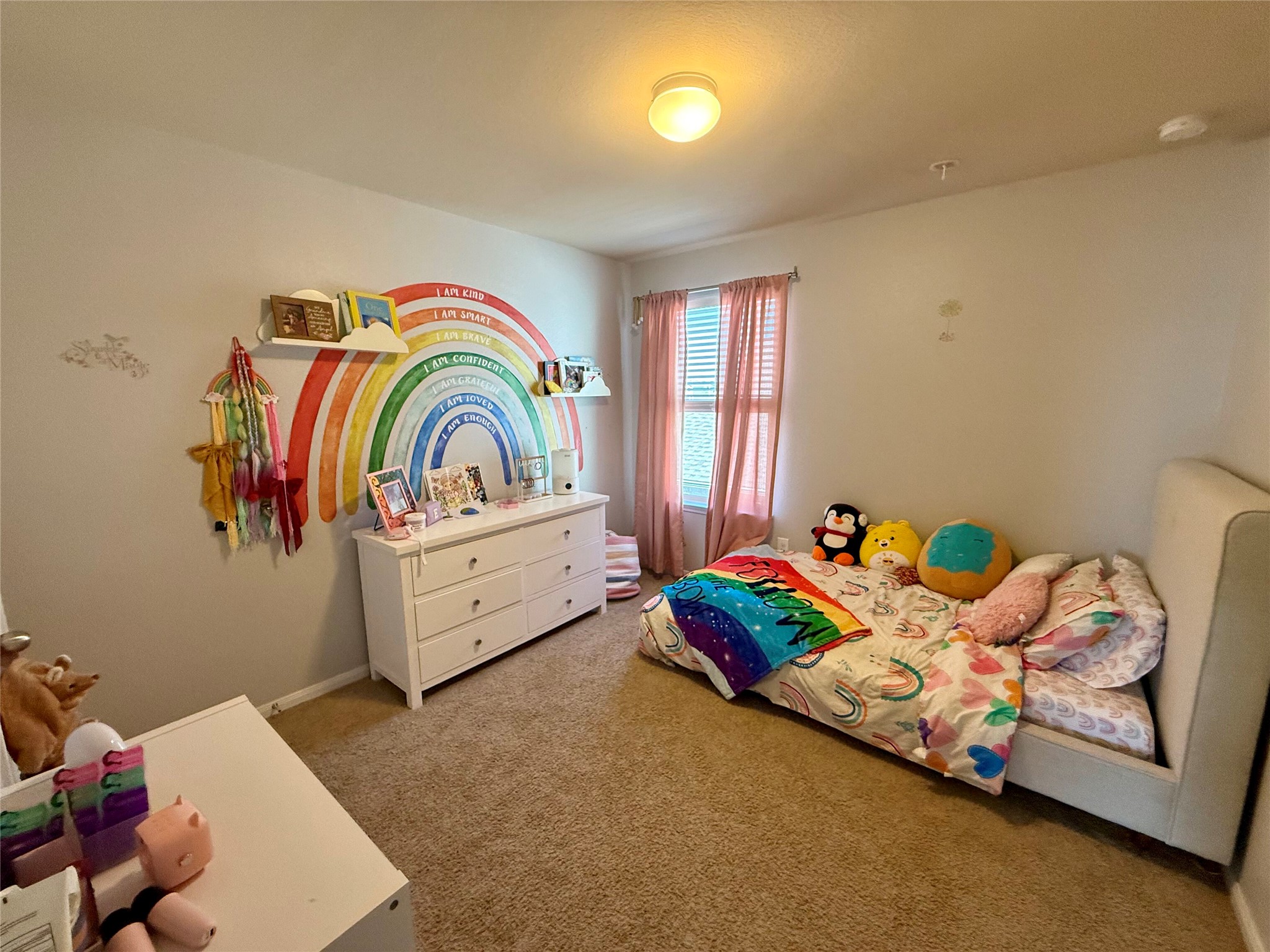 11700 Andesite Road Manor, TX 78653 - Photo 22 of 32 A well-lit bedroom features plush carpet and cheerful rainbow decor, creating a vibrant personal sanctuary.