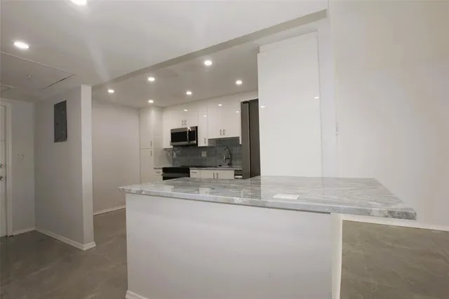 a large white kitchen with stainless steel appliances granite countertop a refrigerator and a stove