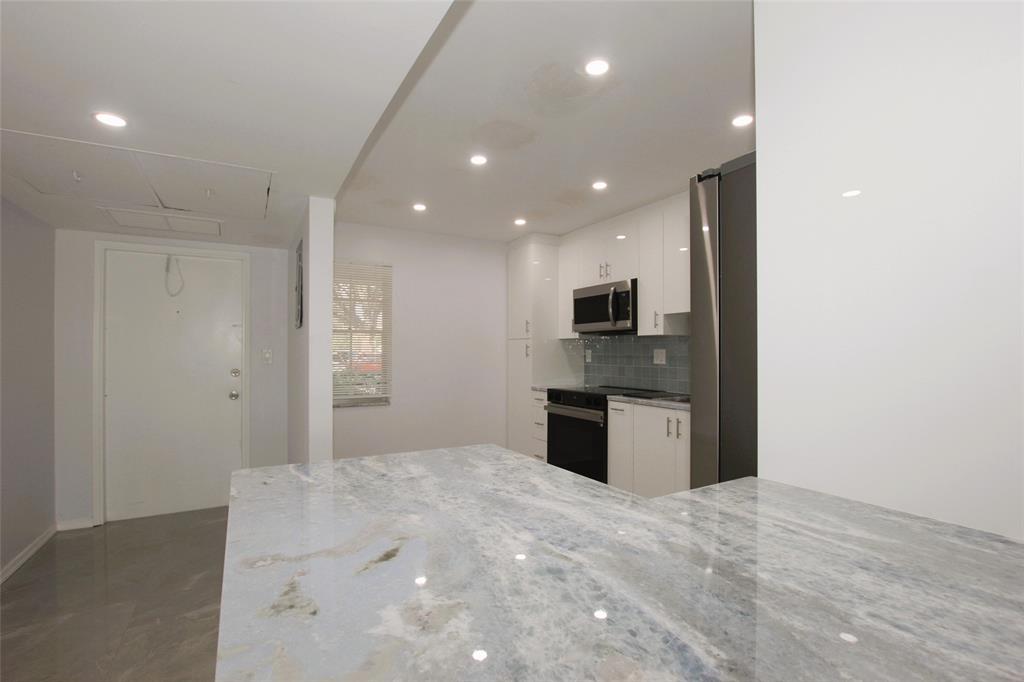 3100 North Course Lane, Unit 103 Pompano Beach, FL 33069 - Photo 10 of 51 a large white kitchen with stainless steel appliances granite countertop a refrigerator and a stove