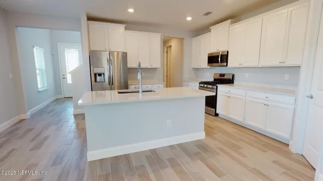 a large kitchen with stainless steel appliances granite countertop a stove a sink a refrigerator and white cabinets with wooden floor