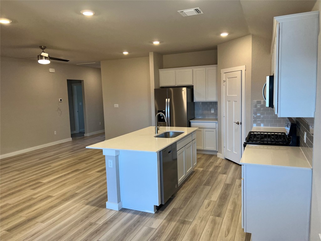404 Coda Crossing Georgetown, TX 78633 - Photo 6 of 15 Kitchen featuring stainless steel appliances, tasteful backsplash, a kitchen island with sink, white cabinets, and light wood-type flooring