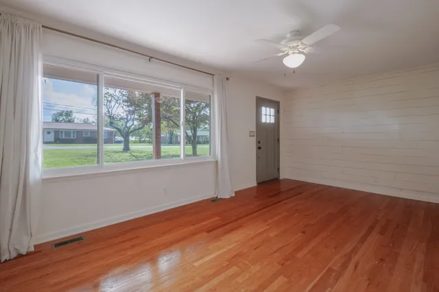 a view of an empty room with wooden floor and a window