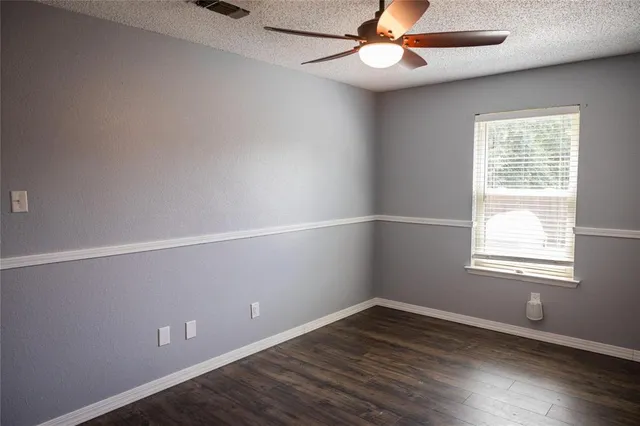 an empty room with wooden floor chandelier fan and windows