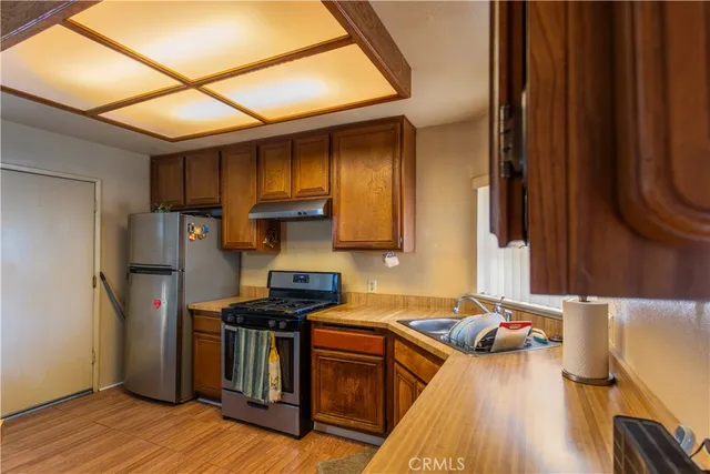 a kitchen with stainless steel appliances granite countertop a refrigerator a sink dishwasher a stove and white countertops with wooden floor