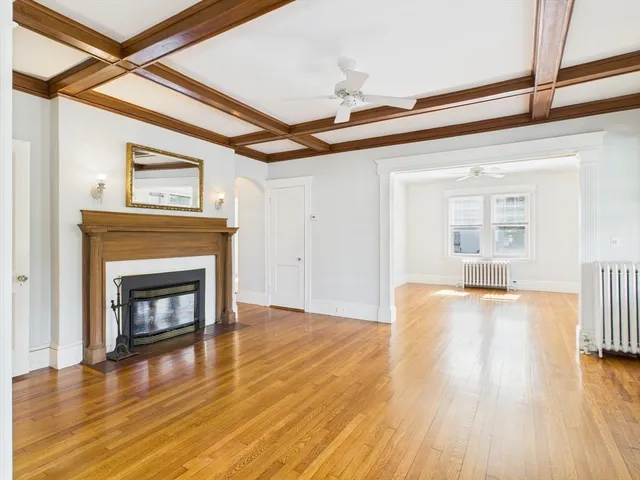 a view of an empty room with wooden floor fireplace and a window