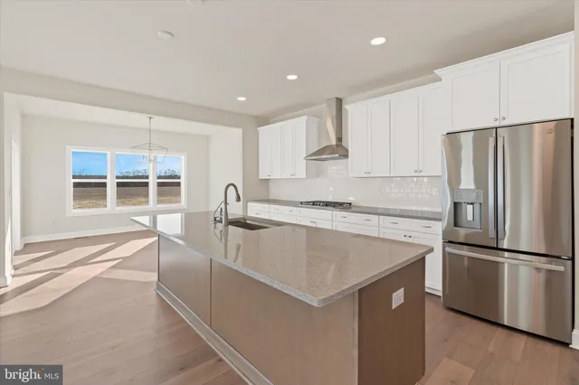 a large kitchen with kitchen island a stove a refrigerator a sink and white cabinets with wooden floor