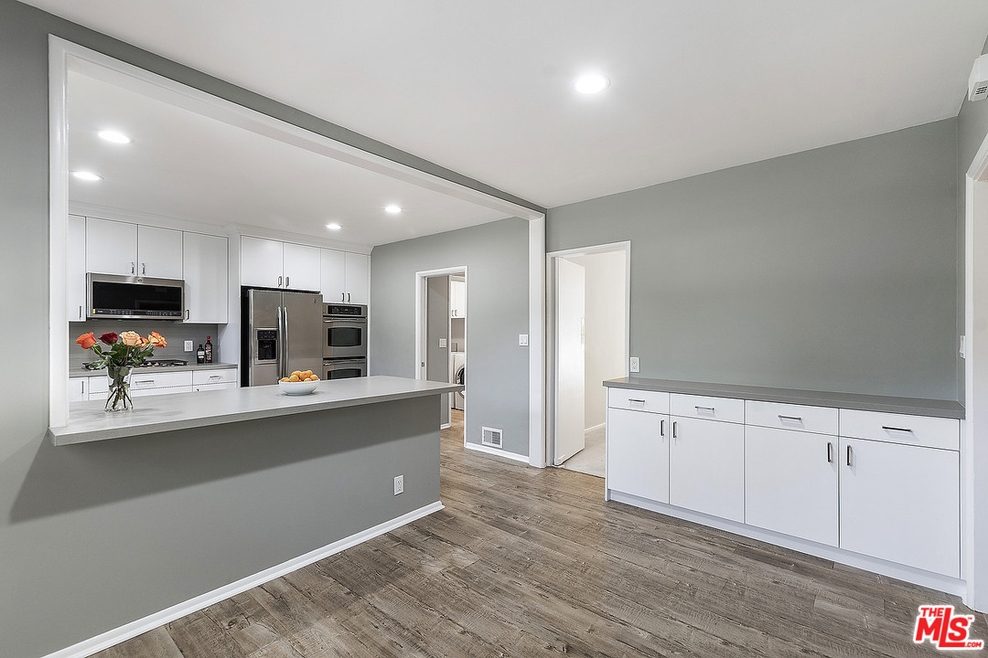 711 Sierra Drive Beverly Hills, CA 90210 - Photo 13 of 40 a large kitchen with stainless steel appliances a large counter top a stove a refrigerator with white cabinets and wooden floor