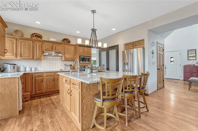 2690 Spaatz Road Monument, CO 80132 - Photo 8 of 50 Kitchen with appliances with stainless steel finishes, light hardwood / wood-style flooring, a center island with sink, and decorative light fixtures