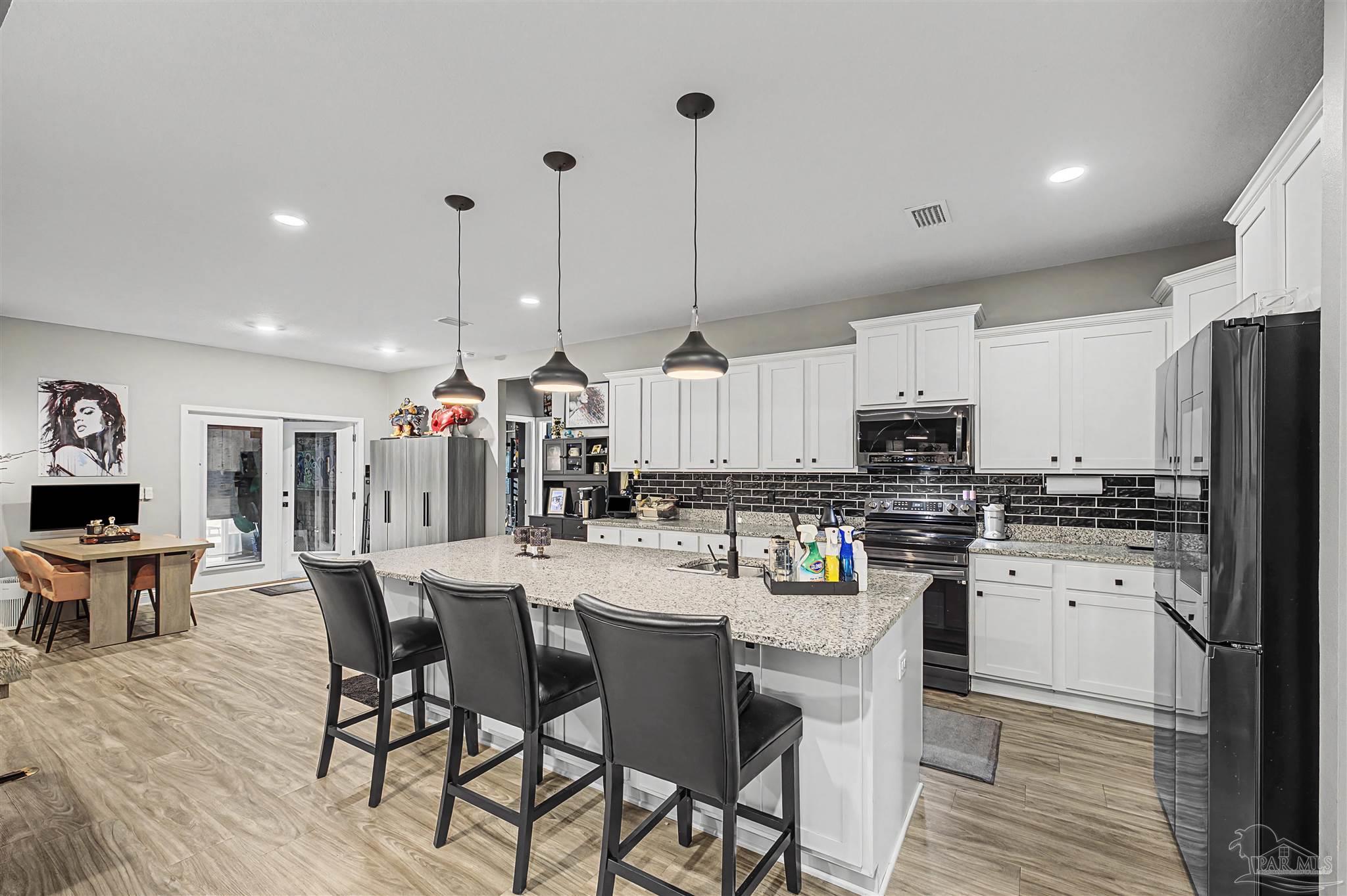 327 Cayden Way Cantonment, FL 32533 - Photo 9 of 64 a kitchen with stainless steel appliances kitchen island granite countertop a dining table chairs and white cabinets