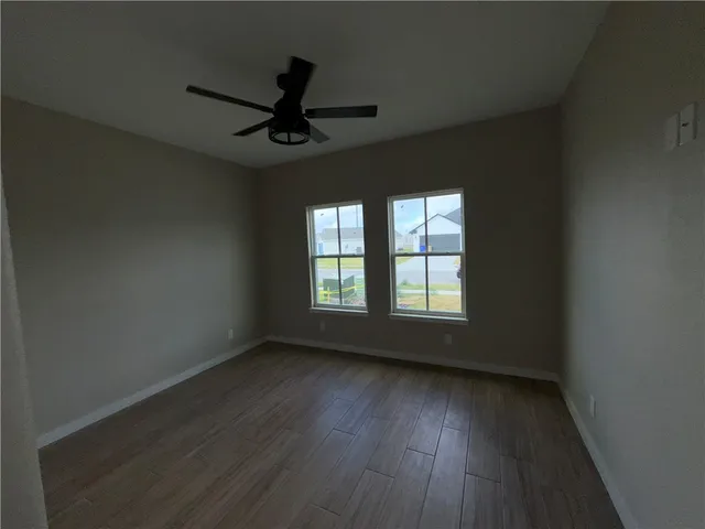 an empty room with wooden floor fan and windows